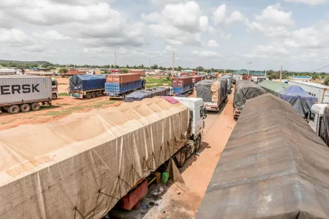 A queue of trucks stretches ten kilometers at the closed Benin-Niger border in Malanville, September 2023, with goods spoiling and drivers facing financial ruin.