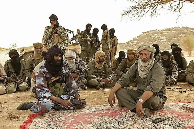 Tuareg rebels sitting on a carpet under a tree, surrounded by fighters.